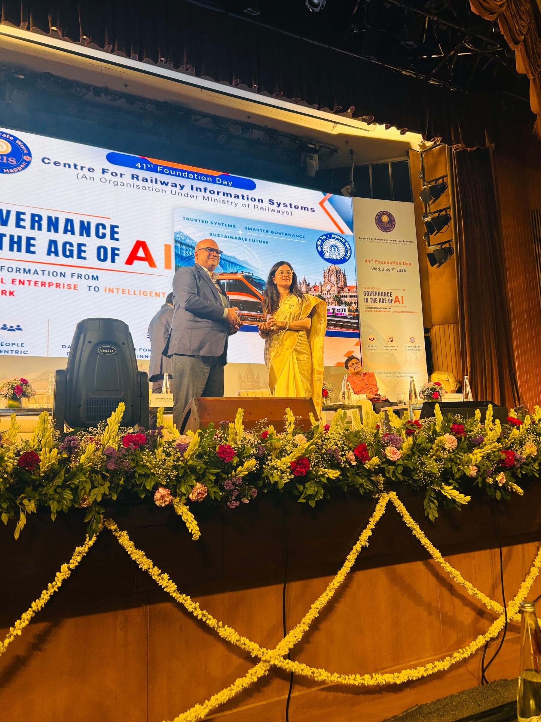 On stage at a conference on governance in the age of AI, standing at the podium beside another speaker under the event banner.