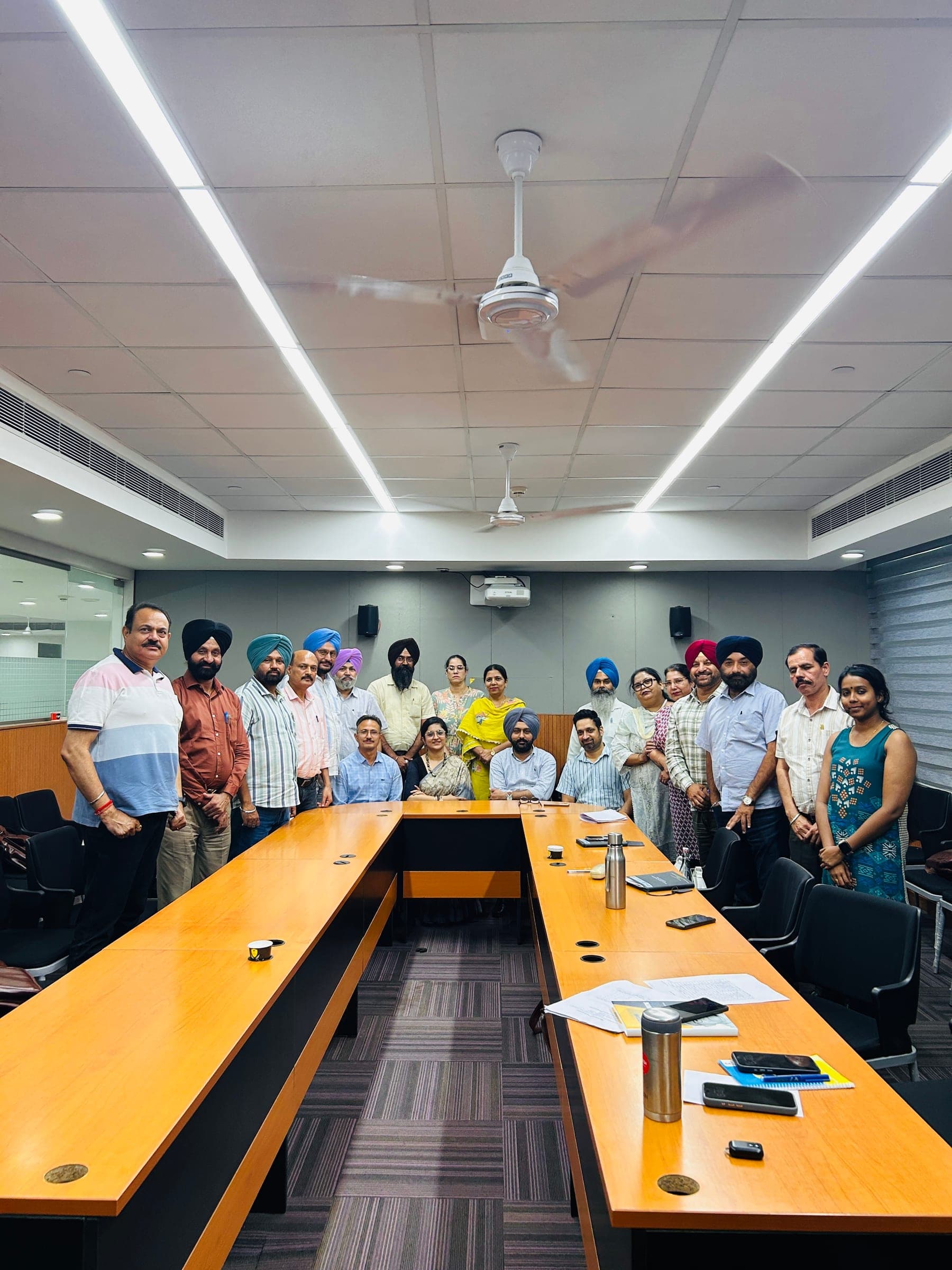 Group photograph at the end of a session, participants standing shoulder to shoulder behind a polished U-shaped seminar table.