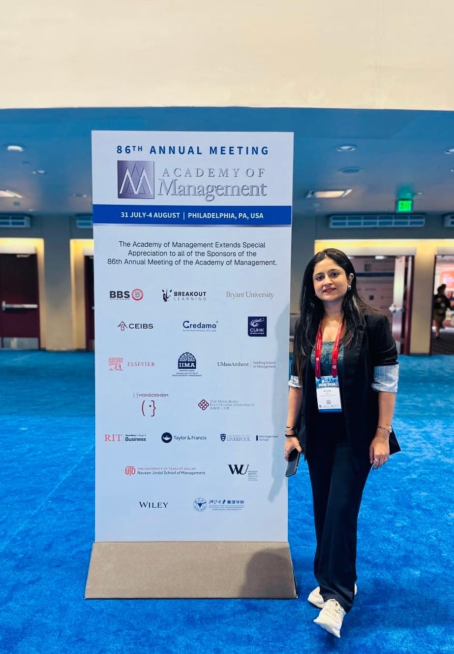 Standing beside the floor-standing signage for the 86th Annual Meeting of the Academy of Management in Philadelphia, wearing a conference lanyard.
